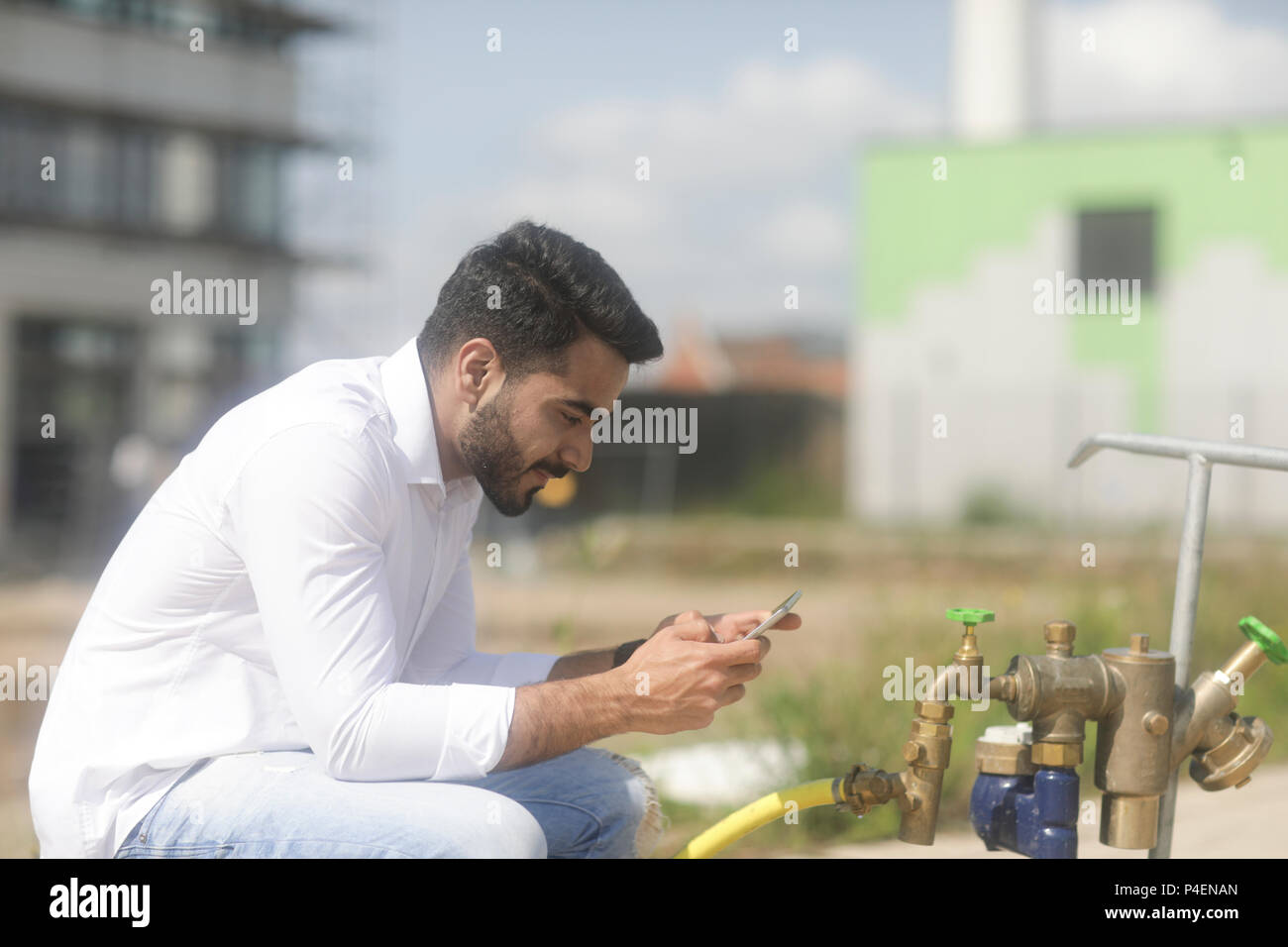 Uomo seduto all'esterno prendendo utilizzando il suo telefono cellulare Foto Stock