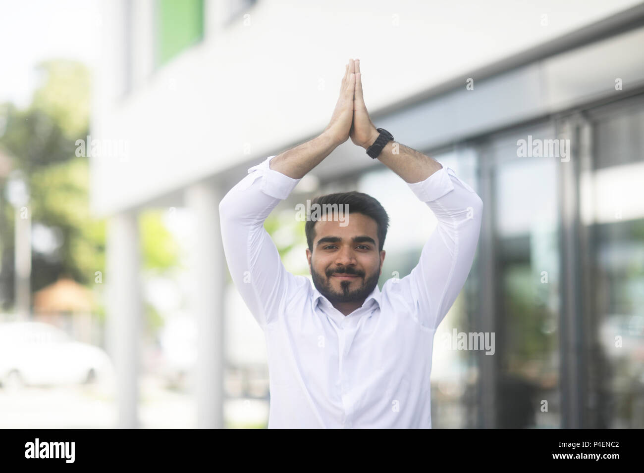 Imprenditore sorridente in piedi all'aperto fare yoga Foto Stock