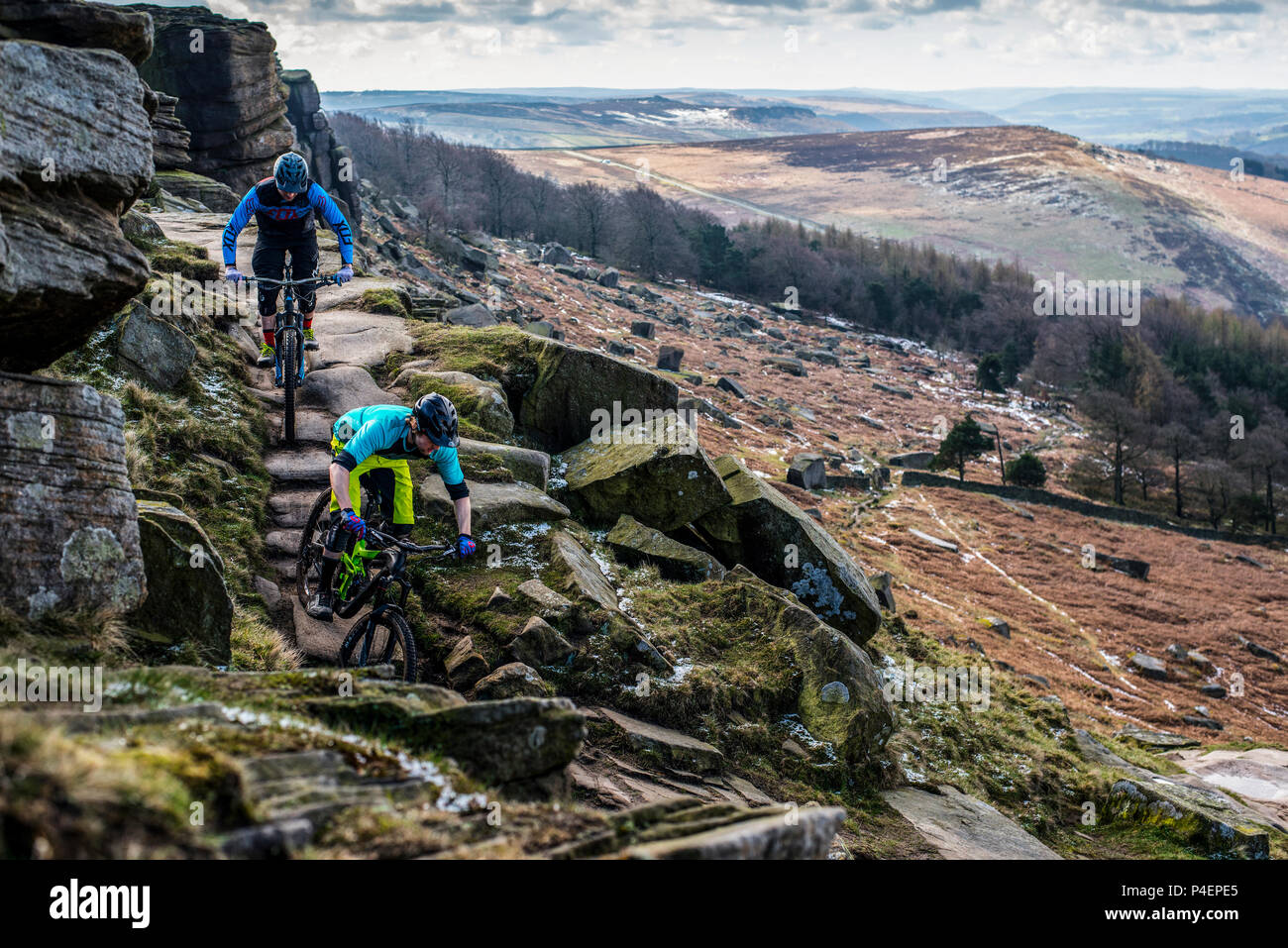 Due uomini in mountain bike cavalcare un sentiero sul bordo Stanage gritstone scogliere, Parco Nazionale di Peak District, Derbyshire. Foto Stock