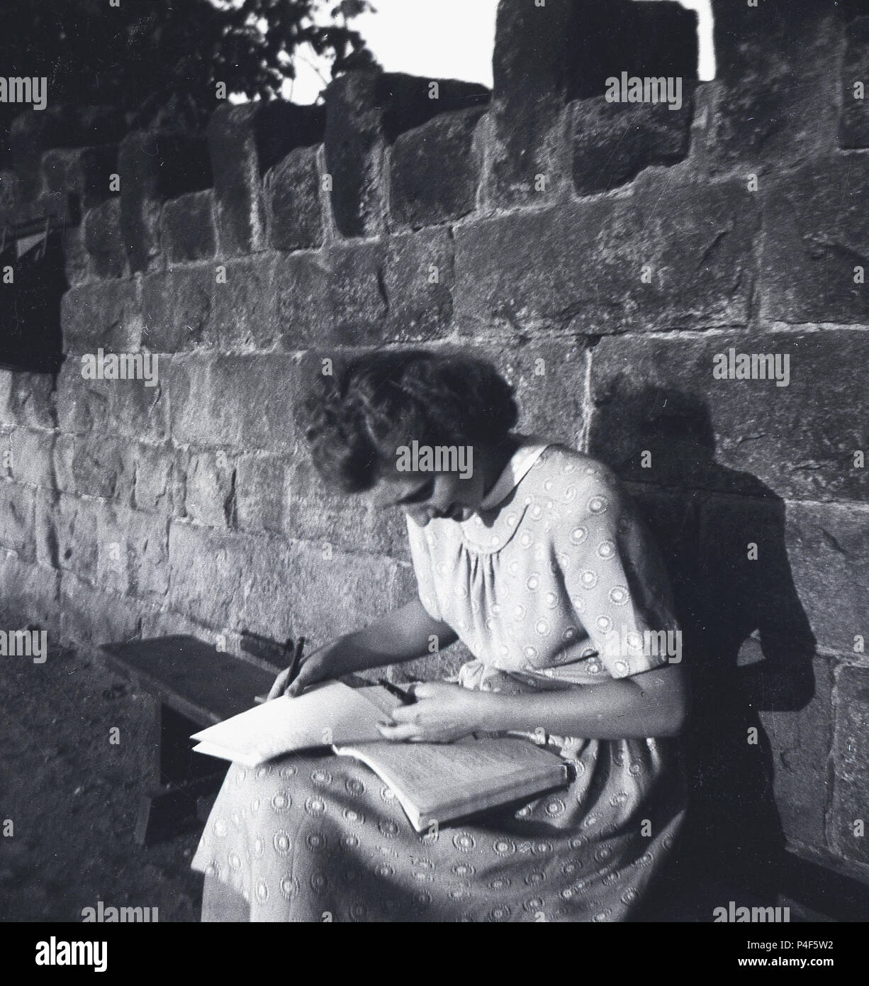 1948, storico post--guerra in Gran Bretagna, la figura mostra una donna giovane, una sesta forma di studente, seduta su una panchina fuori con i suoi libri sul suo grembo e penne a mano, studiare o rivedere il suo lavoro scolastico. Foto Stock