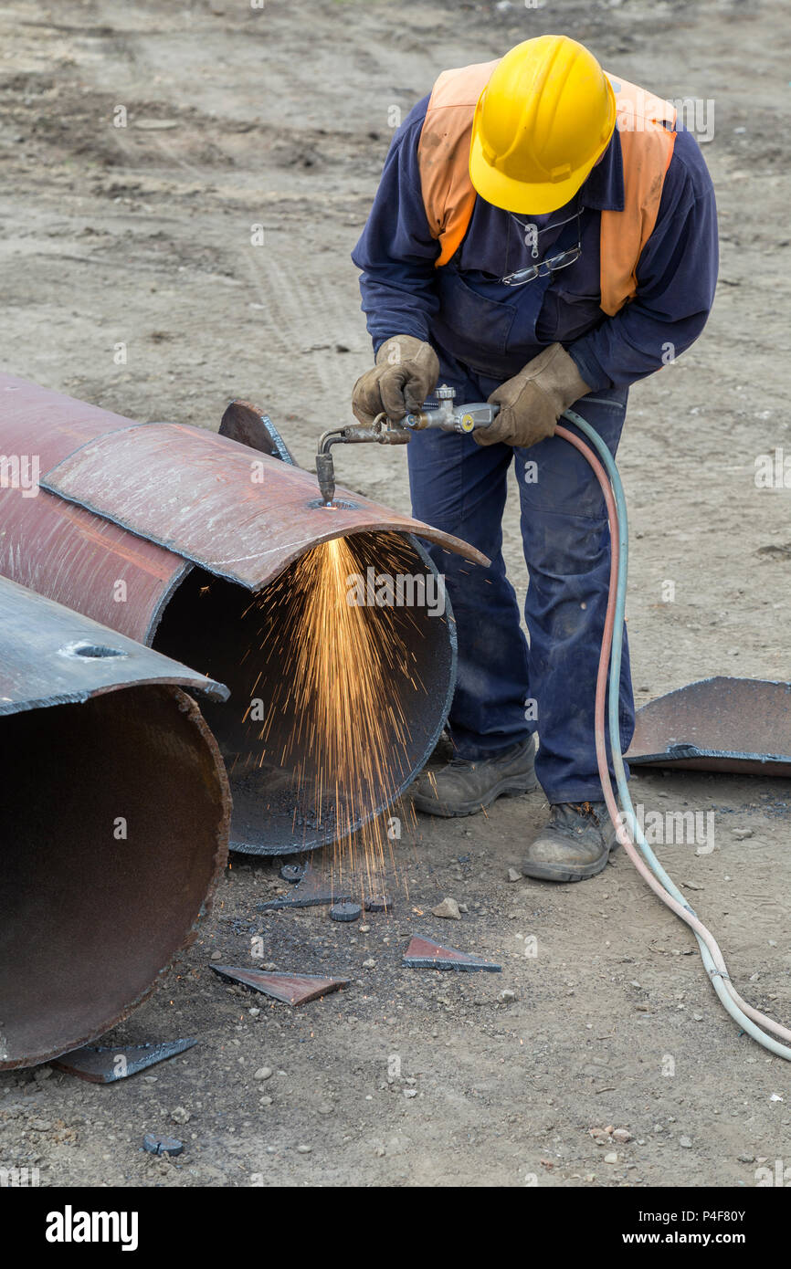Saldatore lavoratore con cannello da taglio, foro di taglio in un tubo in acciaio. Ossigeno-propano cannello da taglio, utilizzato per il taglio di un tubo in acciaio. Foto Stock