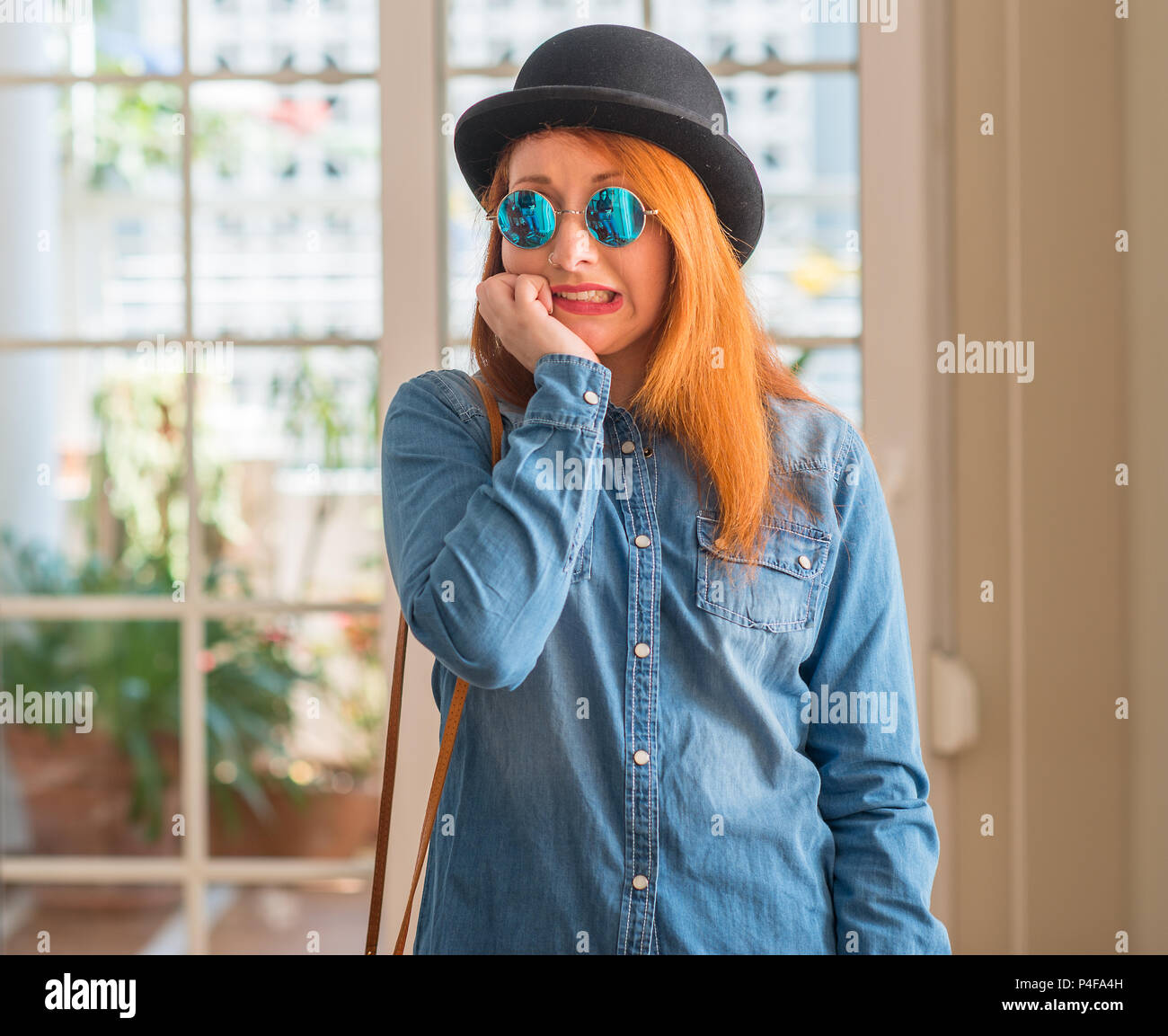 Elegante redhead donna che indossa Bowler cappello e occhiali da sole  cercando stressato e nervoso con le mani sulla bocca di mordere le unghie.  Problema d'ansia Foto stock - Alamy