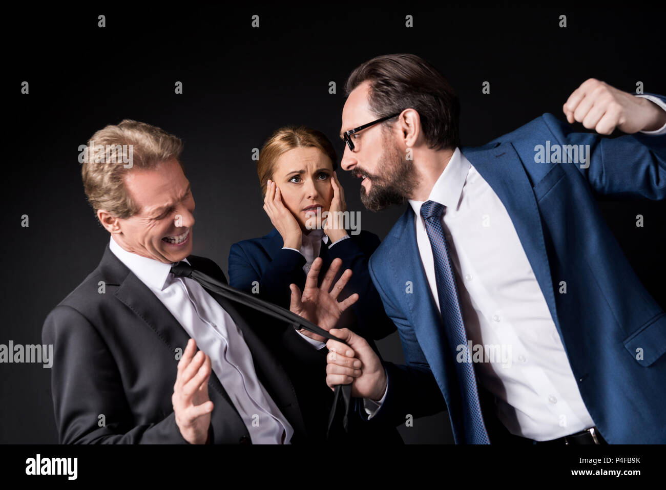 Imprenditori matura lotta mentre spaventata imprenditrice dietro isolato su nero Foto Stock