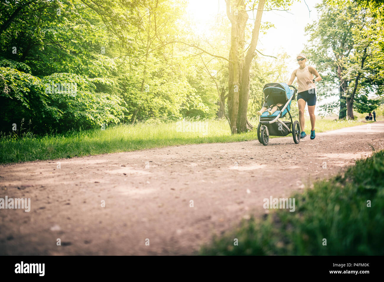 Esecuzione di donna con passeggino godendo giornata estiva nel parco. Il jogging o power walking supermom, active famiglia con bambino pareggiatore. Foto Stock
