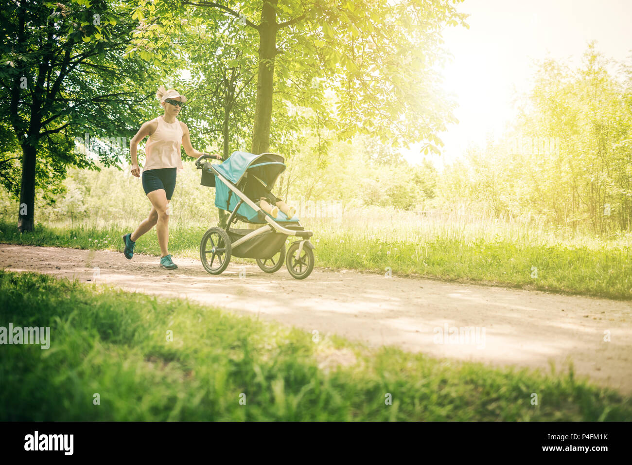 Esecuzione di donna con passeggino godendo giornata estiva nel parco. Il jogging o power walking supermom, active famiglia con bambino pareggiatore. Foto Stock