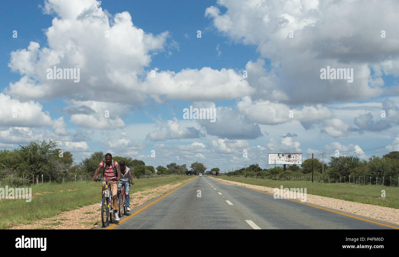 Paesaggio rurale del Capo Nord, Sudafrica con due ciclisti neri africani maschi su una strada quasi vuota che si estende fino alla distanza Foto Stock