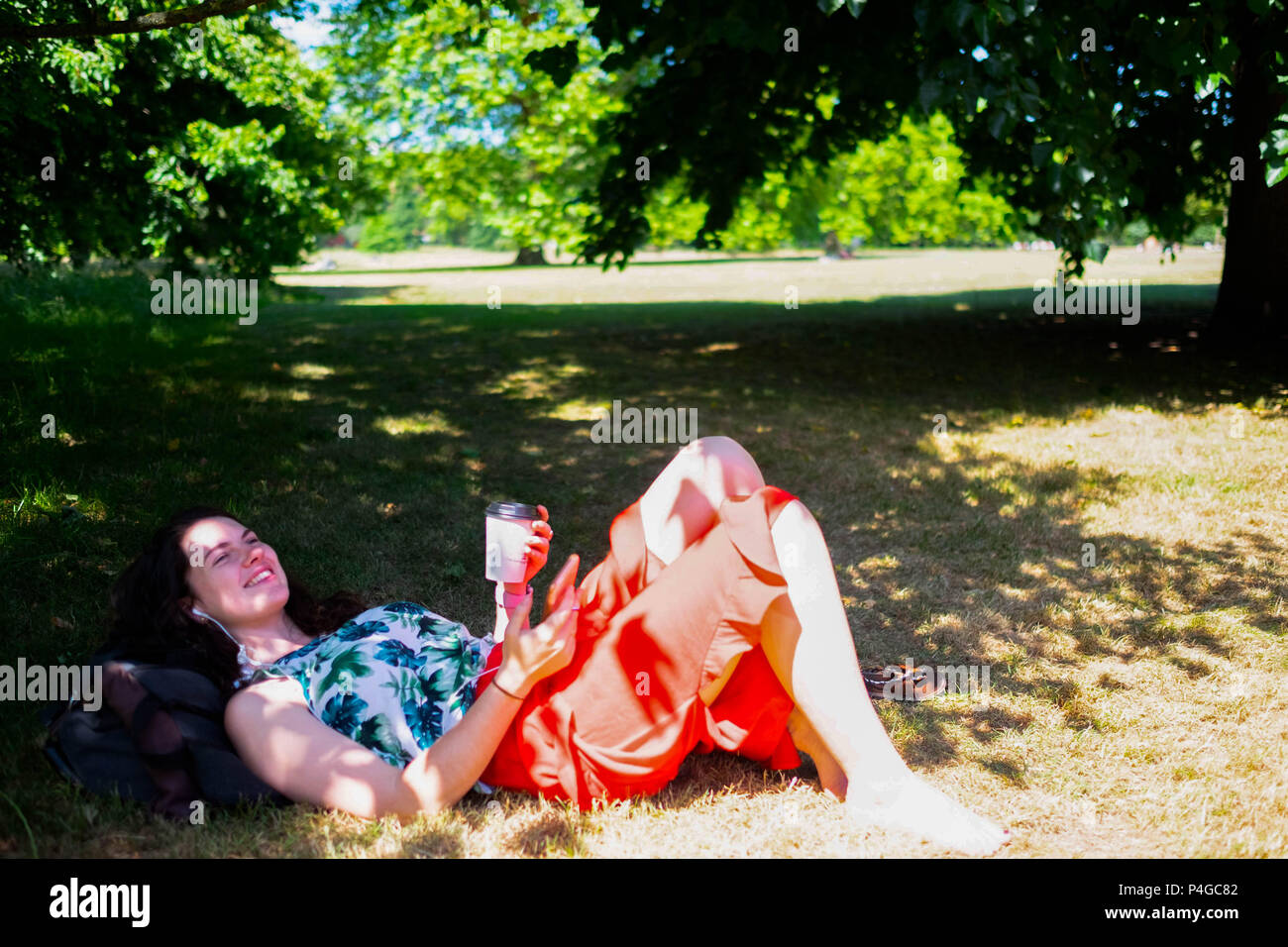 Londra, Inghilterra. Il 22 giugno 2018. Louise Craker, 22, trova qualche ombra dove si può ascoltare la sua musica e bere il caffè,in Hyde Park in un posto molto soleggiato giorno a Londra. Questo tempo soleggiato è detto di continuare per i prossimi giorni. ©Tim anello/Alamy Live News Foto Stock