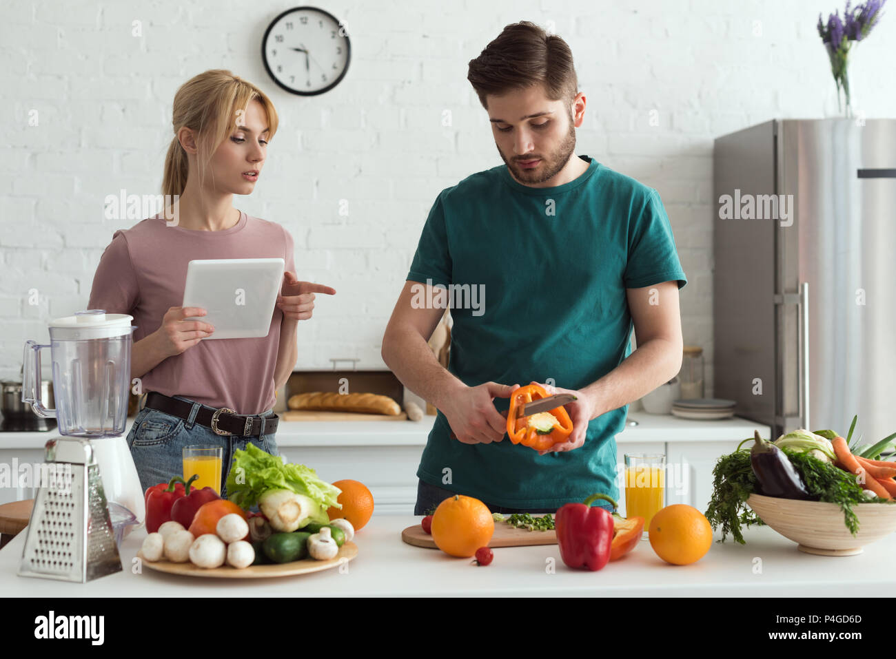 Paio di vegetariani utilizzando tablet con ricetta per la cottura in cucina Foto Stock