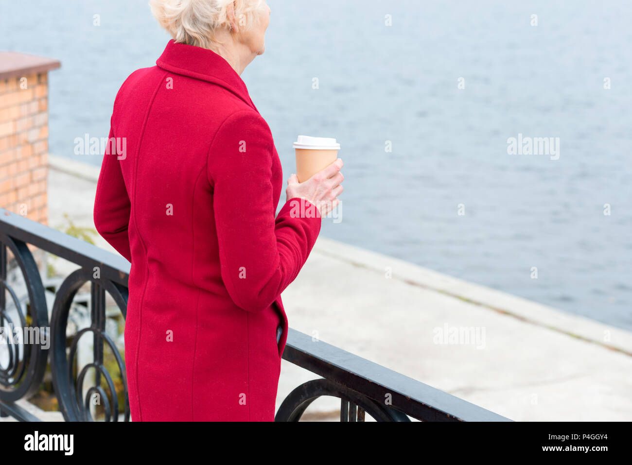 Vista ritagliata della senior woman in red coat con caffè di andare in banchina Foto Stock