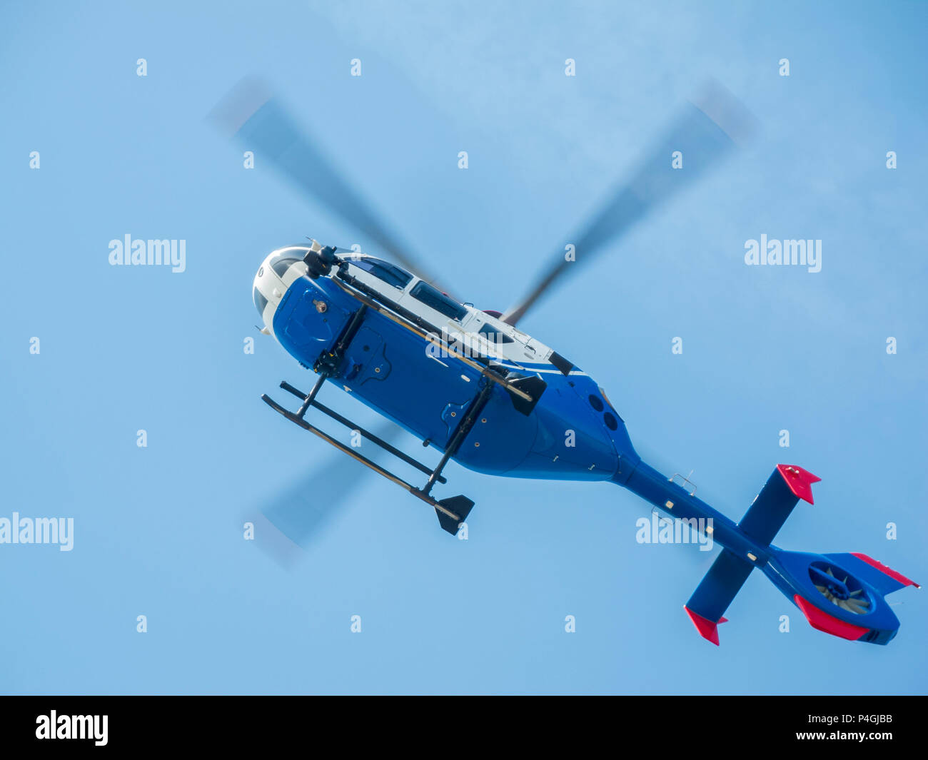 Al di sopra della fotocamera blu hovering elicottero con leggermente sfuocate le pale del rotore contro un cielo blu in vista inferiore. Foto Stock