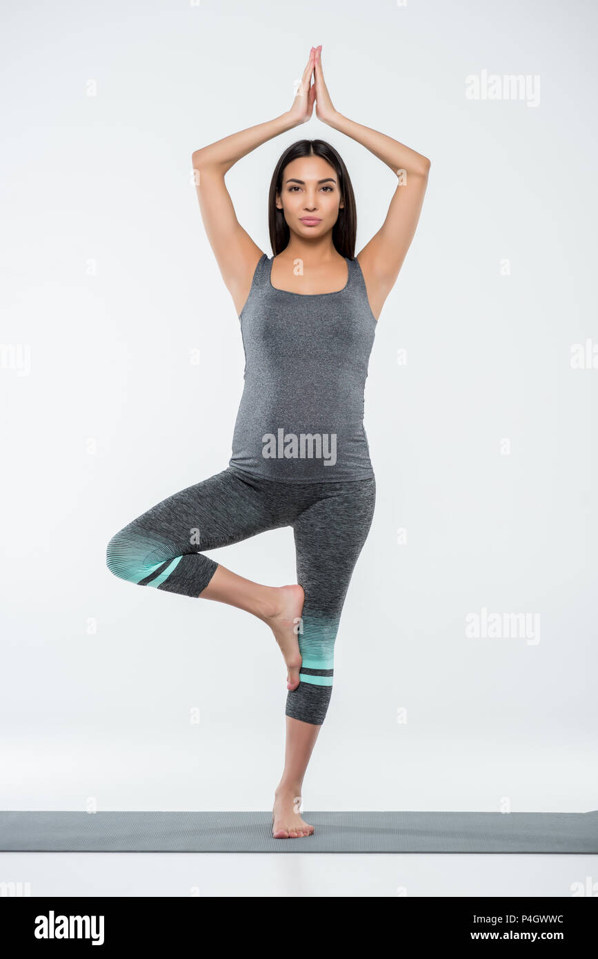 Asian donna incinta a praticare yoga in posa ad albero, isolato su grigio Foto Stock