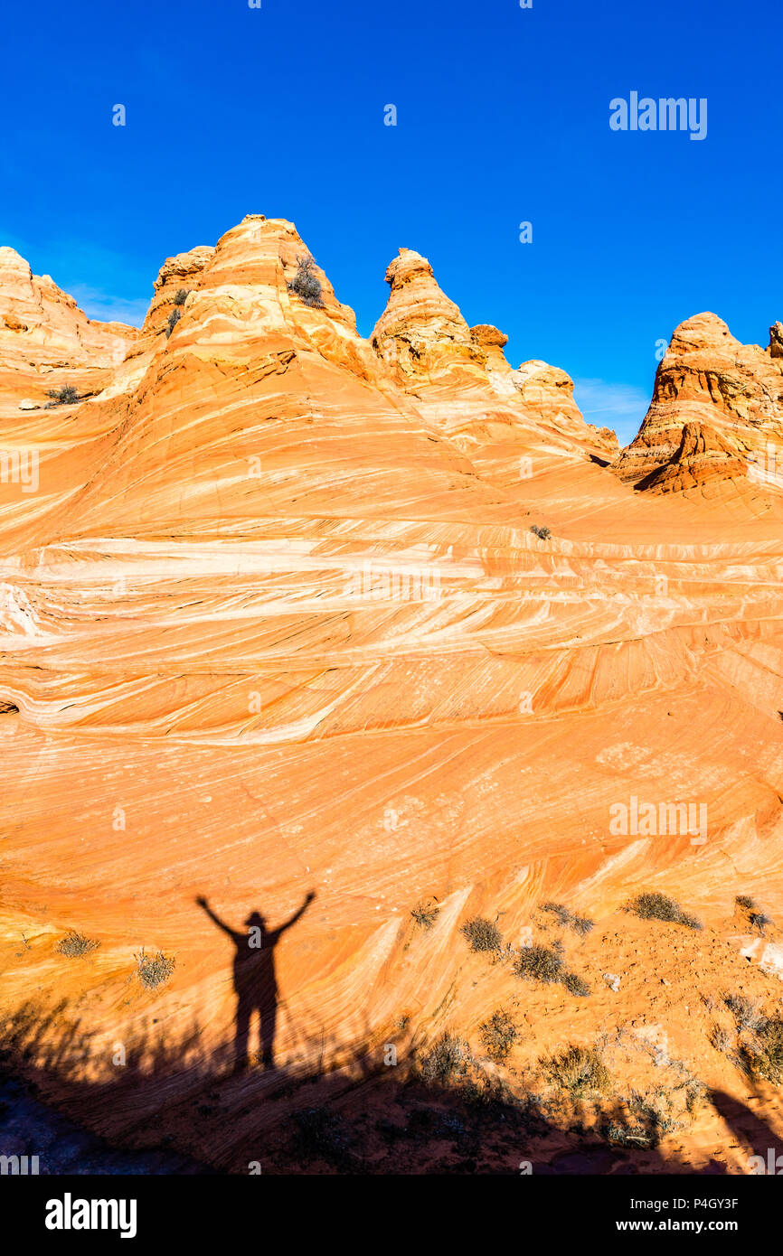 Ombra di un uomo con le braccia tese visualizzata su pietra arenaria rossa tepee formazioni Sud Coyote Buttes area scogliere Vermiglio monumento nazionale, AZ Foto Stock