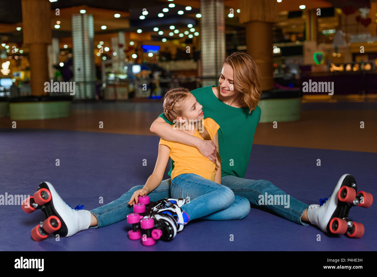 Sorridente madre e figlia piccola seduta sul rullo rink insieme Foto Stock