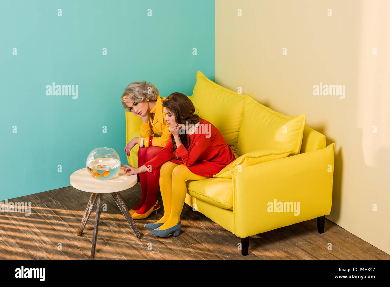 In stile retrò le donne sedute sul divano giallo con pesci di acquario sul tavolino a colorato appartamento, casa di bambola concept Foto Stock