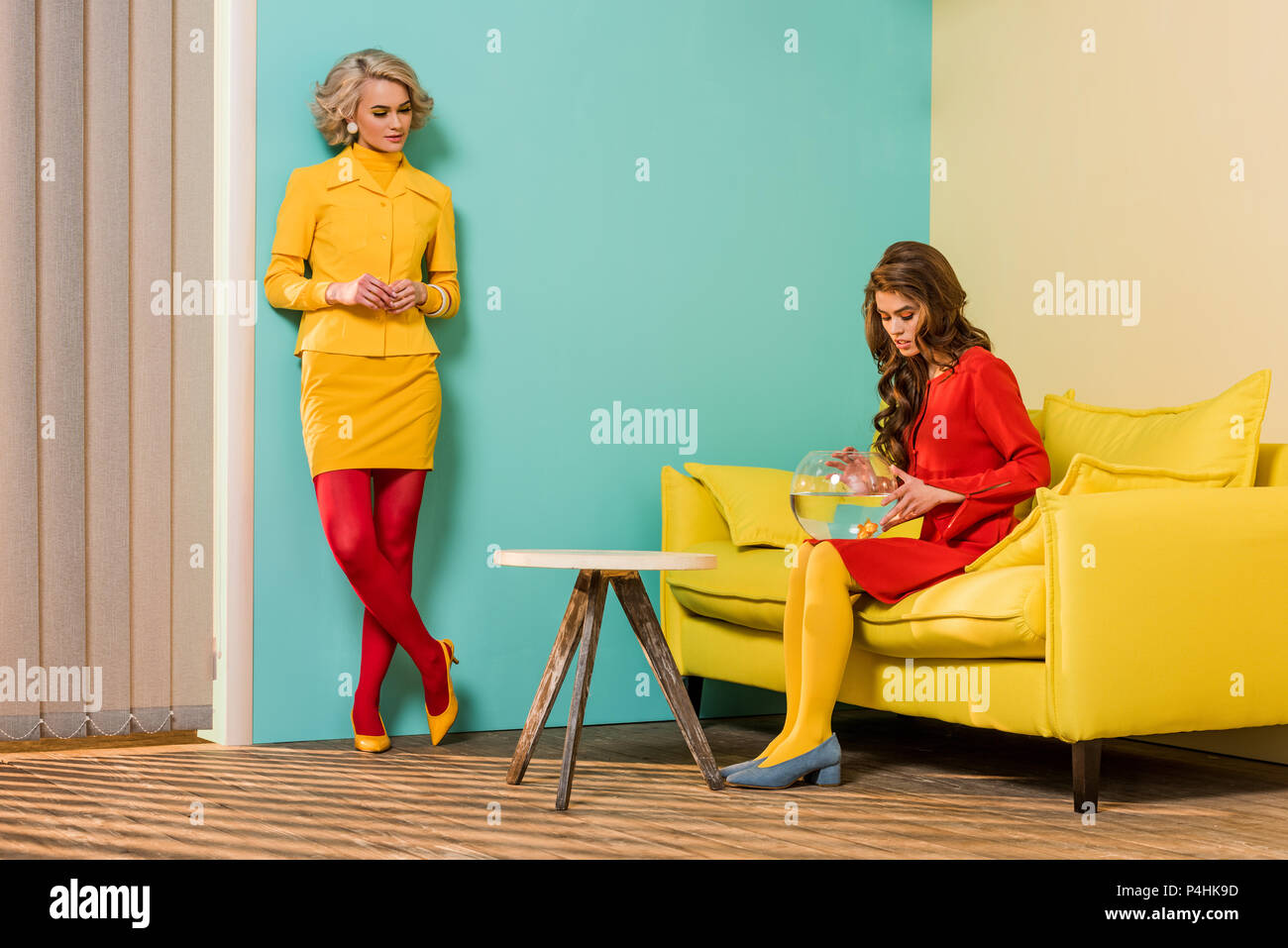 Giovani in stile retrò donne in appartamento colorato con divano giallo e pesci di acquario, casa di bambola concept Foto Stock