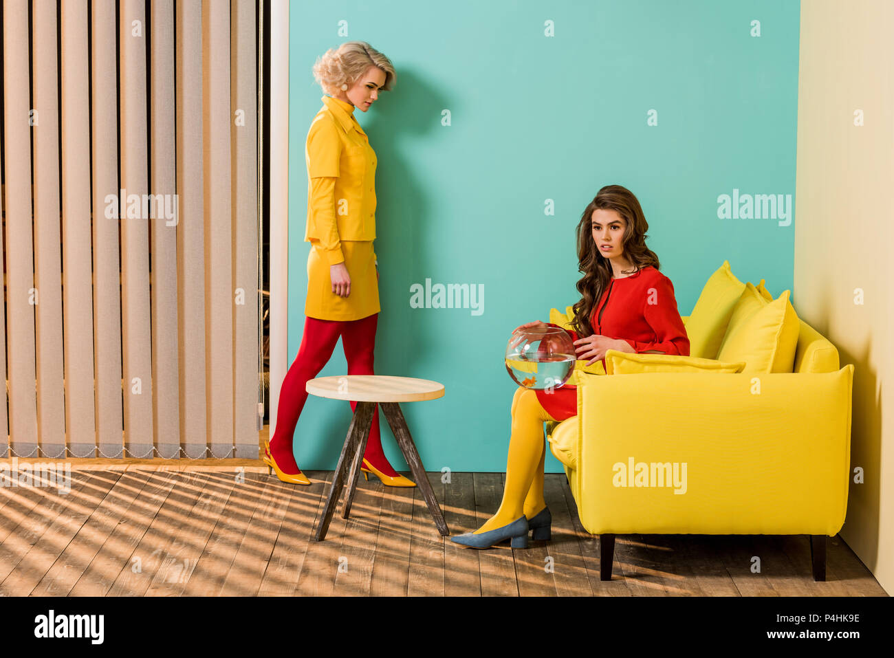 Giovani in stile retrò donne in appartamento colorato con divano giallo e pesci di acquario, casa di bambola concept Foto Stock