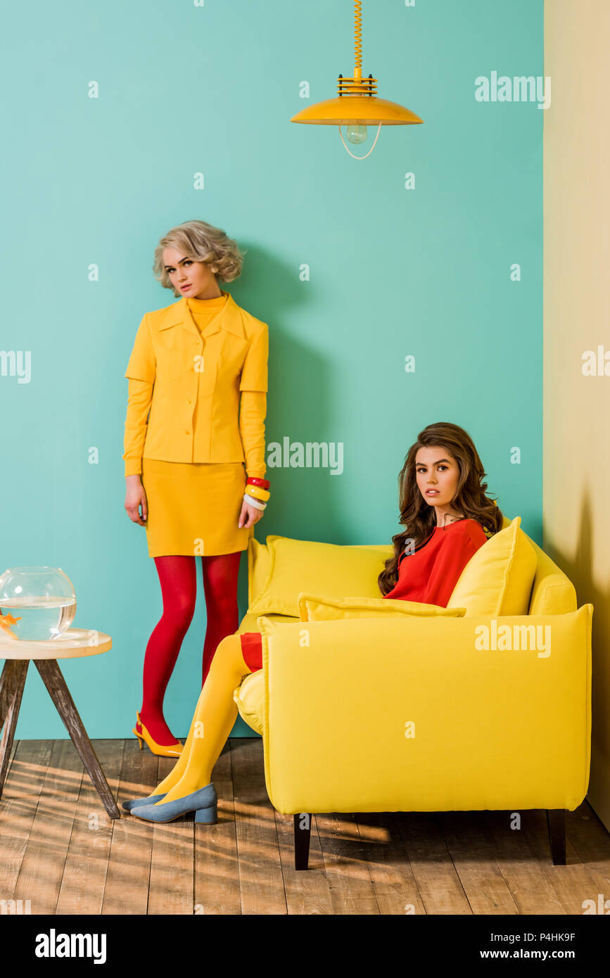 Giovani in stile retrò donne in appartamento colorato con divano giallo e pesci di acquario, casa di bambola concept Foto Stock