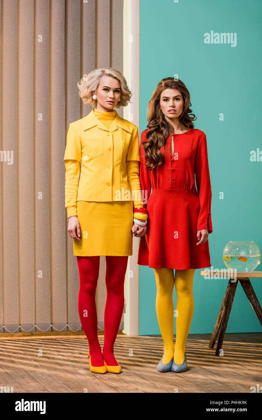 Le donne in luminosi in stile retrò abbigliamento tenendo le mani al colorato appartamento, casa di bambola concept Foto Stock