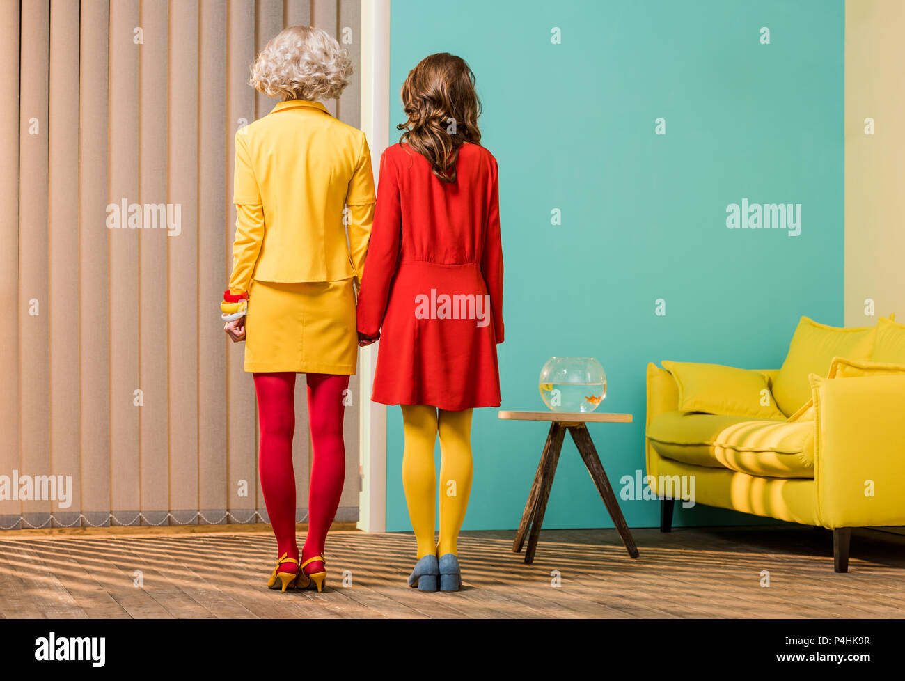 Vista posteriore delle donne in luminosi in stile retrò abbigliamento tenendo le mani al colorato appartamento, casa di bambola concept Foto Stock