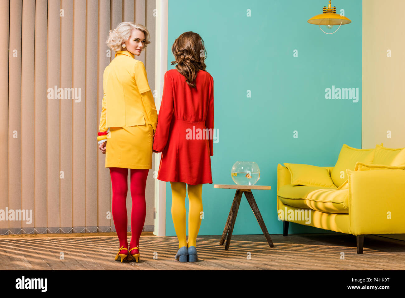 Vista posteriore delle donne in luminosi in stile retrò abbigliamento tenendo le mani al colorato appartamento, casa di bambola concept Foto Stock
