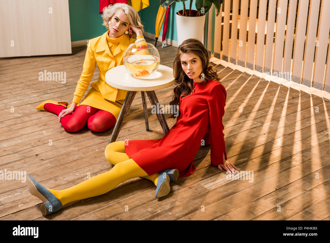 Giovani in stile retrò le donne sedute sul pavimento vicino a golden fish in acquario su un tavolo da caffè, casa di bambola concept Foto Stock