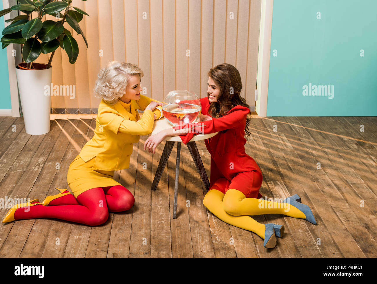 Sorridente in stile retrò le donne sedute sul pavimento vicino a golden fish in acquario su un tavolo da caffè, casa di bambola concept Foto Stock