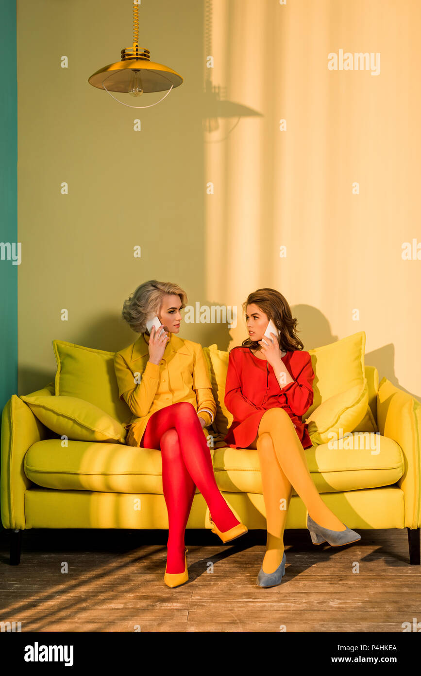 In stile retrò donne parlare su smartphone sul divano giallo, casa di bambola concept Foto Stock
