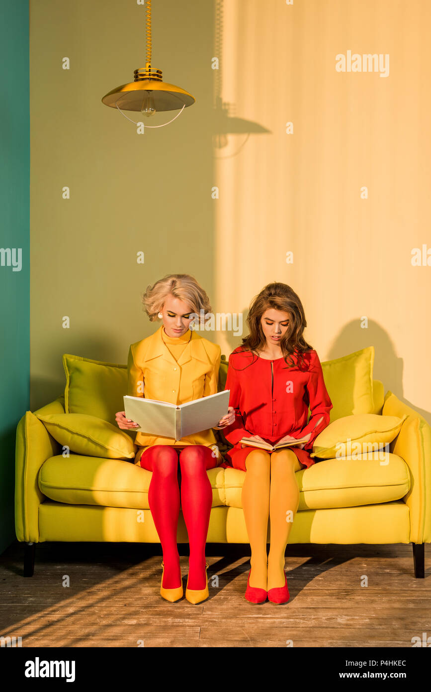 Le donne in abbigliamento retrò la lettura di libri seduti sul divano giallo a luminoso appartamento, casa di bambola concept Foto Stock
