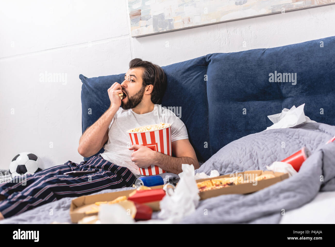 Bel solitario mangiare popcorn e guardare la tv in camera da letto Foto Stock