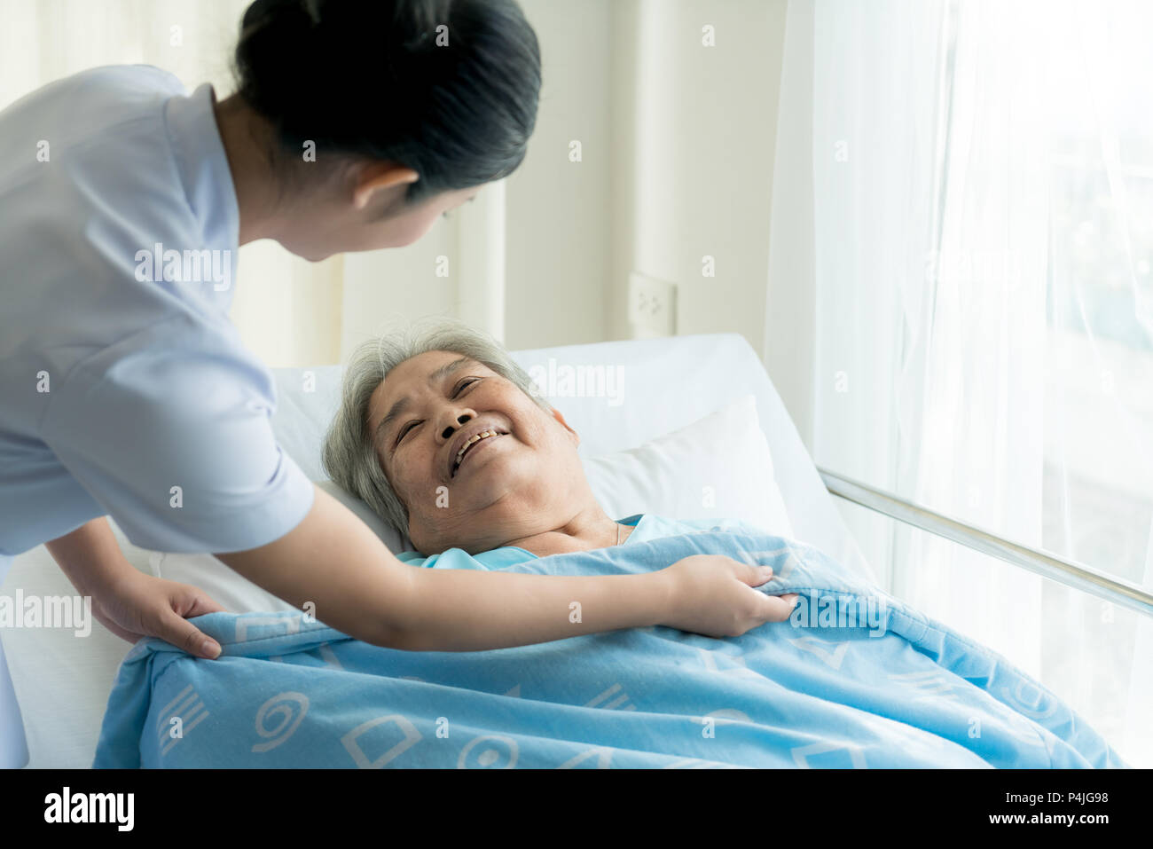 Asian infermiera in assistenza agli anziani coprirla con una coperta per gli anziani in casa di riposo. Foto Stock