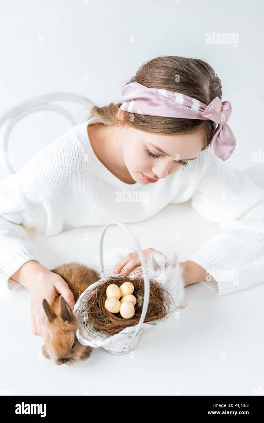 Angolo di alta vista della ragazza guardando i conigli e la cesta con uova di pasqua nel nido Foto Stock