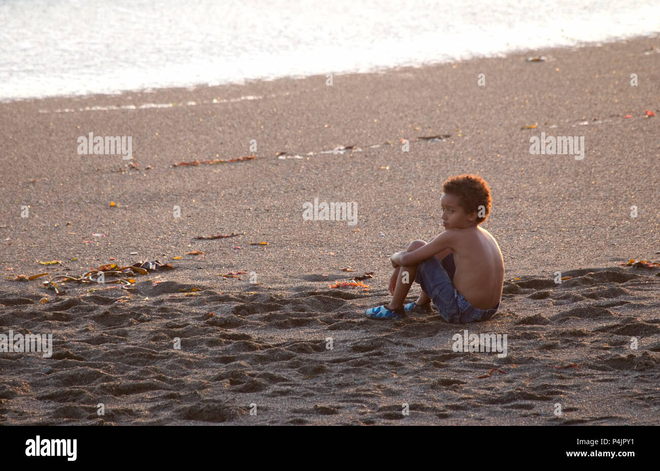 La minoranza giovane ragazzo seduto da solo sulla spiaggia Foto Stock