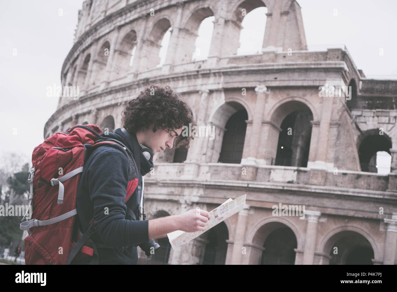 Vintage cerca immagine del bel giovane viaggiatore guardando la mappa turistica di Roma davanti al Colosseo. Zaino in spalla con la fotocamera e la mappa turistica Foto Stock