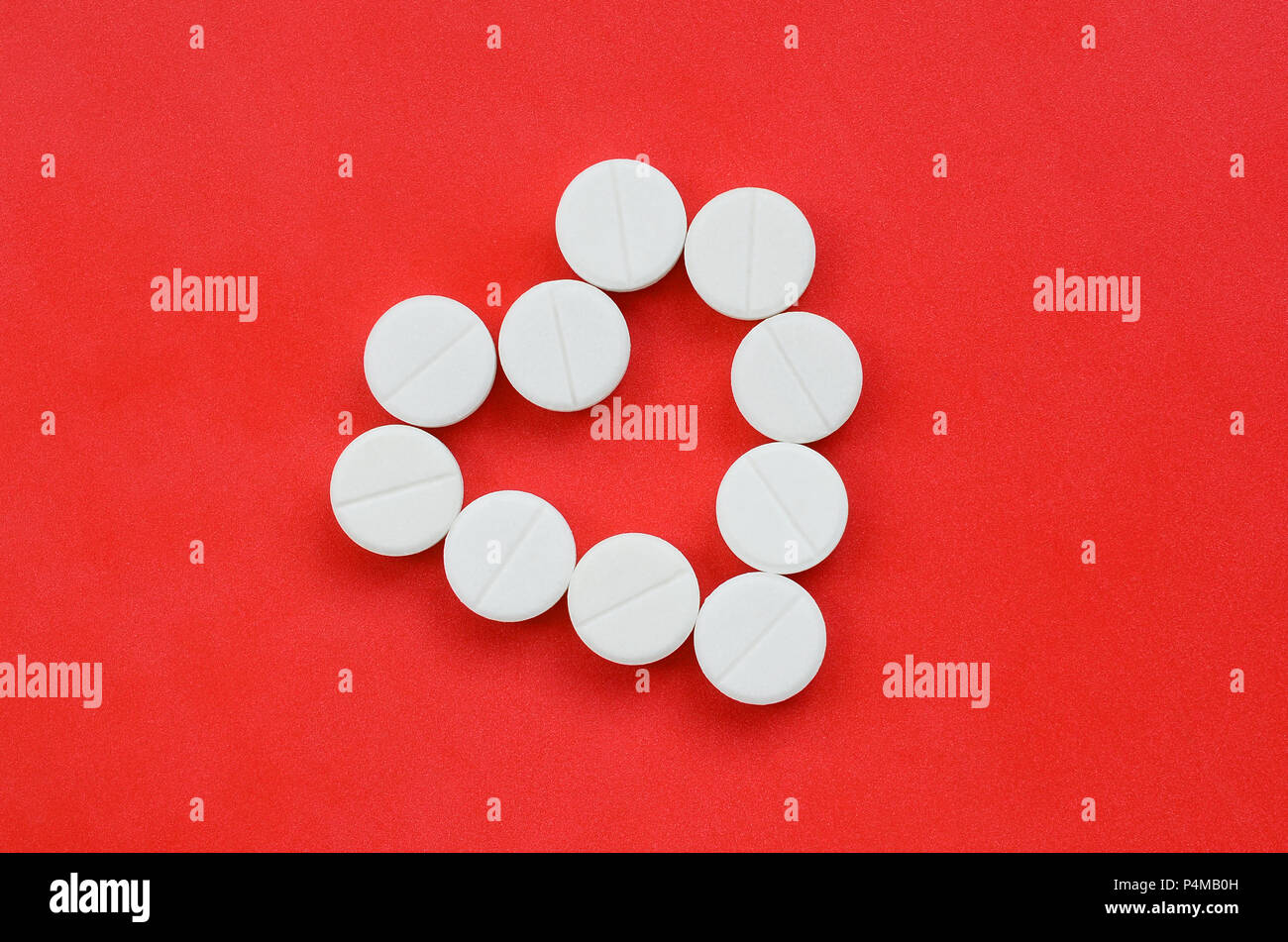 Diverse compresse bianche giacciono su un brillante sfondo rosso a forma di cuore. Immagine di sfondo sulla medicina e argomenti farmaceutiche . Foto Stock