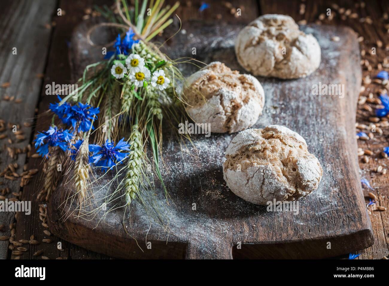 Un sano pane integrale panini con spighe di grano e fiori di campo su una tavola di legno Foto Stock