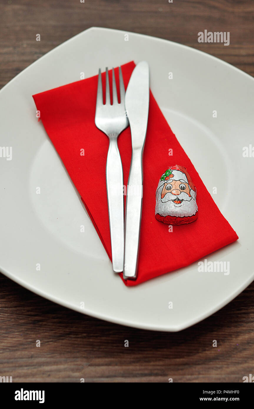 Una semplice impostazione del luogo per il Natale costituito da una piastra, forcella, coltello, rosso igienico e un cioccolato avvolto con un Babbo Natale del volto Foto Stock