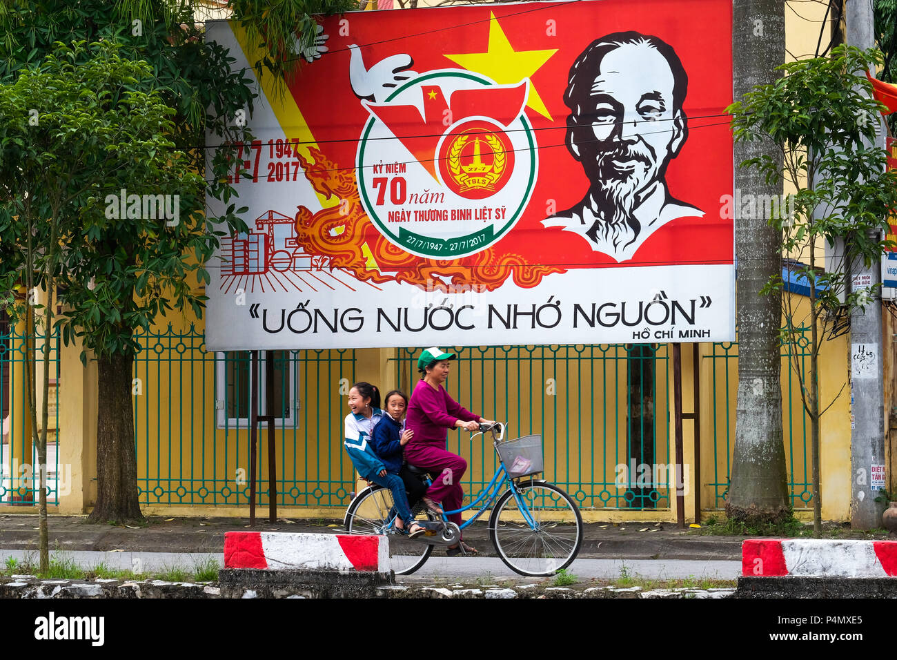 La donna in sella ad una bicicletta sotto un Vietnam Partito Comunista poster di propaganda nella provincia di Nam Dinh, Vietnam - Propagandaplakat der kommunistischen Partei Vietnams in der Nam Dinh-Provinz, Vietnam Foto Stock