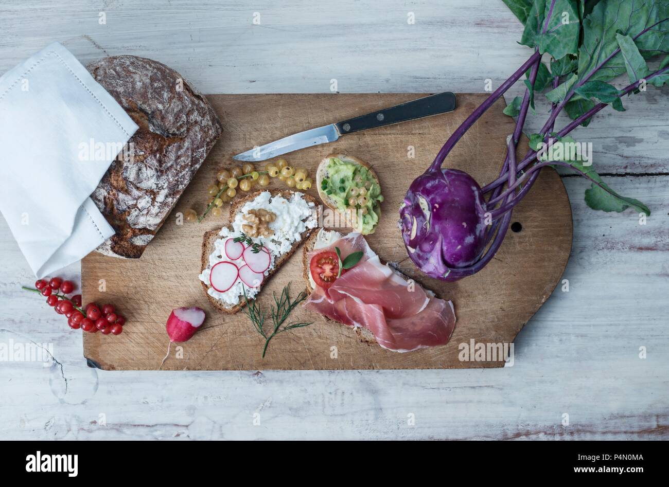 Fette di pane con vari ingredienti su di un tagliere con ribes rosso, viola il cavolo rapa e crosta di pane Foto Stock