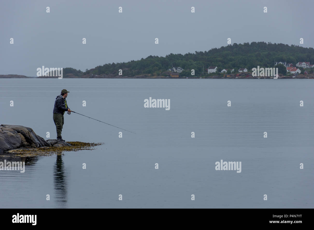 Il pescatore ricreativo in verde waders la filatura per la trota di mare in un suono norvegese - acque costiere. Foto Stock