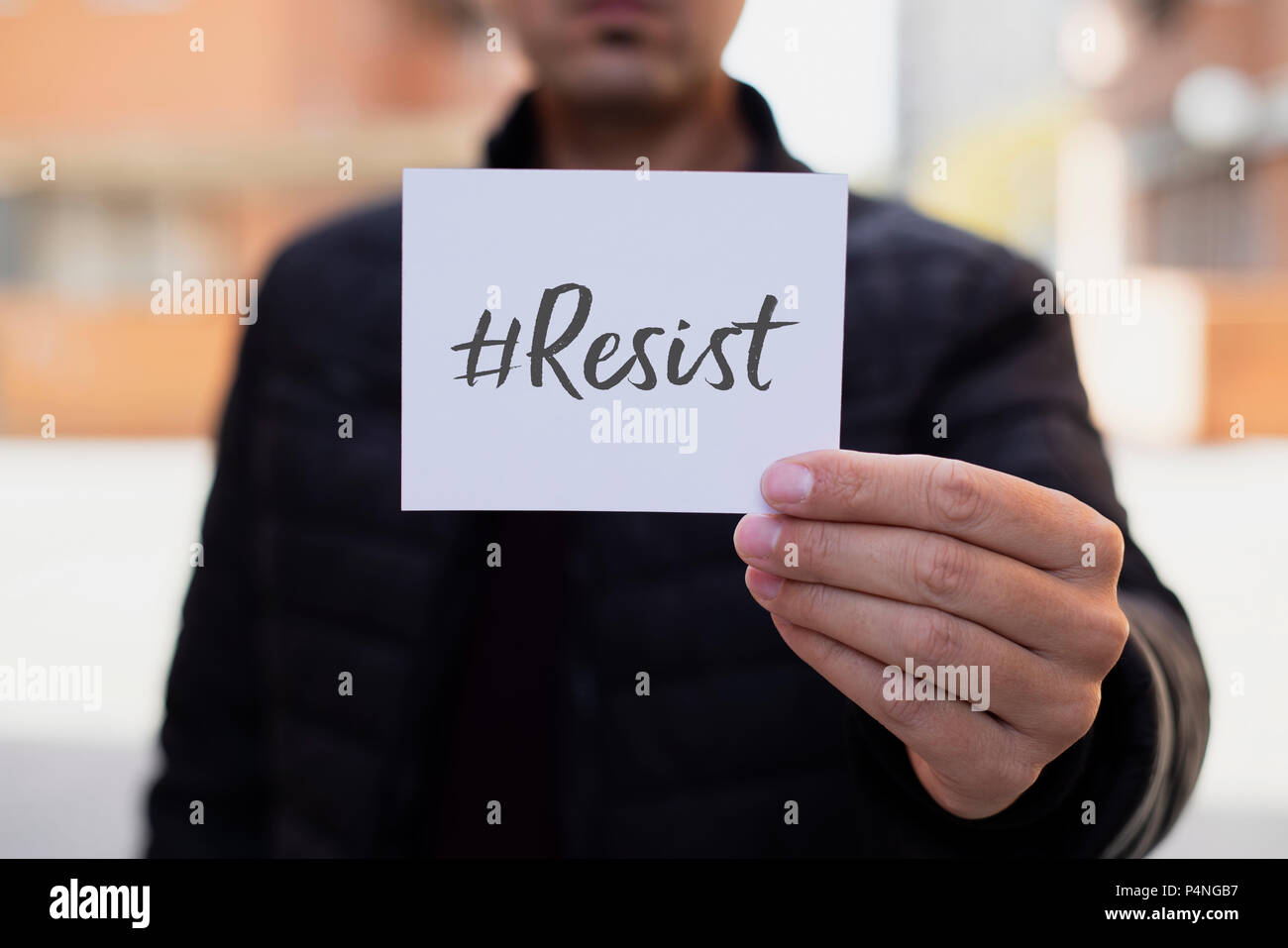 Primo piano di un giovane uomo caucasico, sulla strada, che mostra un pezzo di carta con il resist hashtag scritto in esso Foto Stock
