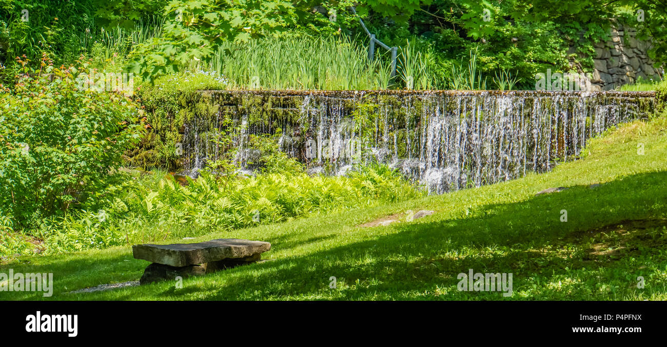 Banco di pietra sul percorso con acqua che cade fuori vecchio muro lungo il ruscello Foto Stock