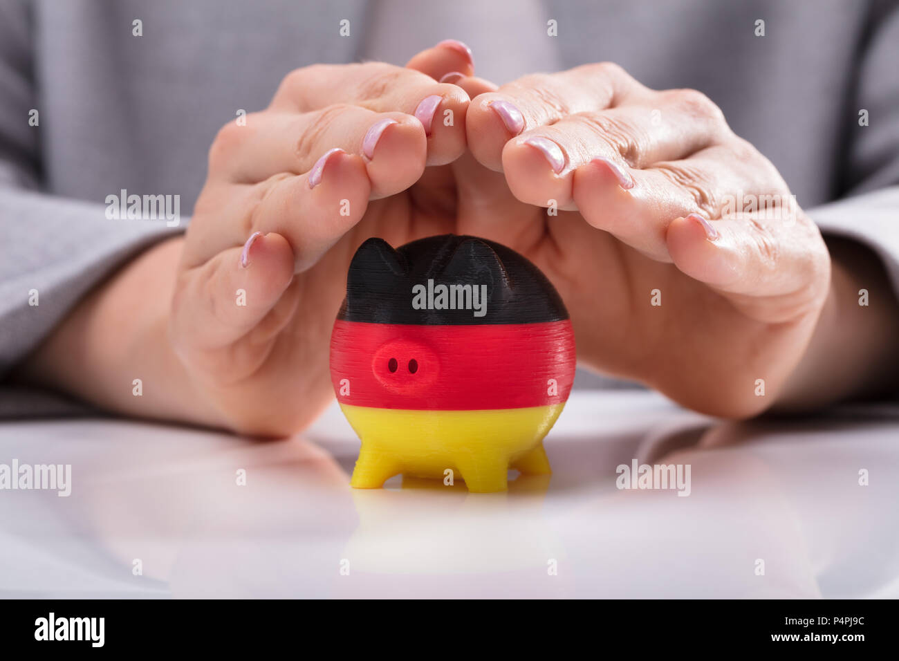 Close-up di una donna di mano proteggere Piggybank dipinta con bandiera tedesca sulla scrivania Foto Stock