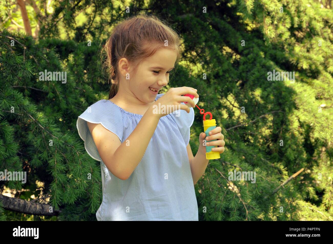 Carino capelli biondi girl, preparando a soffiare le bolle di acqua nel parco, verdi alberi di sfondo, il fuoco selettivo, spazio di copia Foto Stock