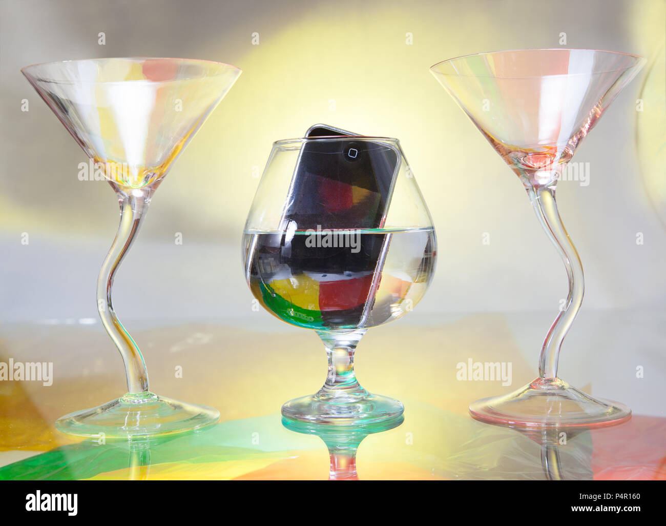 In centro, è possibile vedere un brandy di vetro in cui un telefono cellulare è immerso. Due bicchieri da cocktail inquadrare la scena Foto Stock