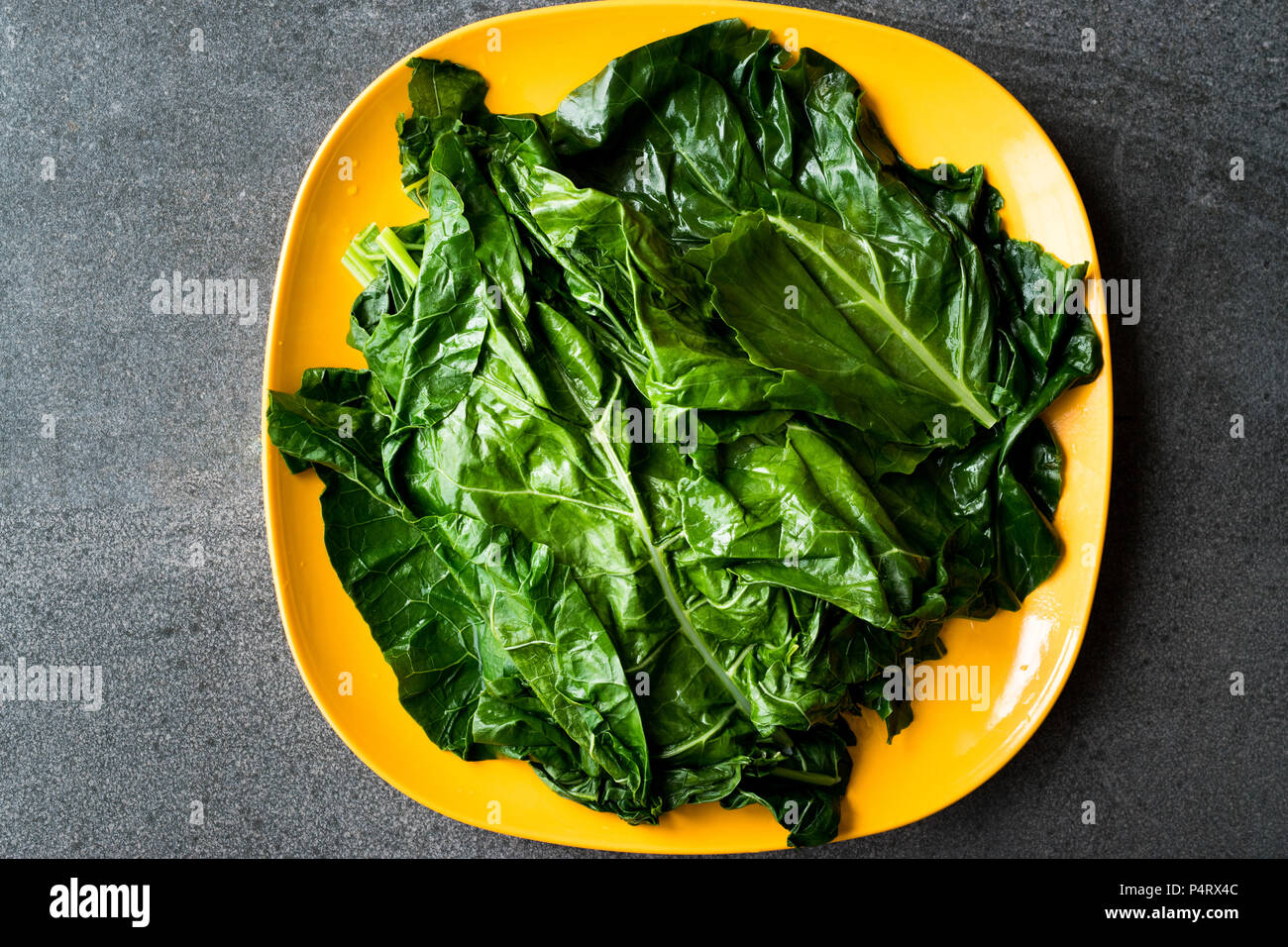 Cavolo nero foglie / Verde biologico Lacinato Kale sulla piastra di colore giallo con granito grigio superficie. Alimenti biologici. Foto Stock