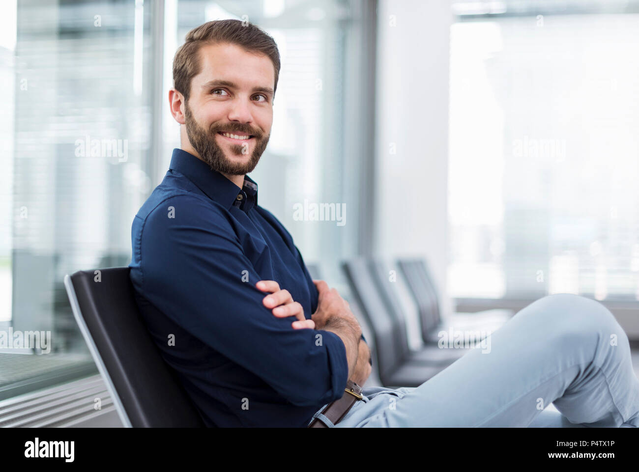 Sorridente imprenditore giovane seduto in area di attesa Foto Stock