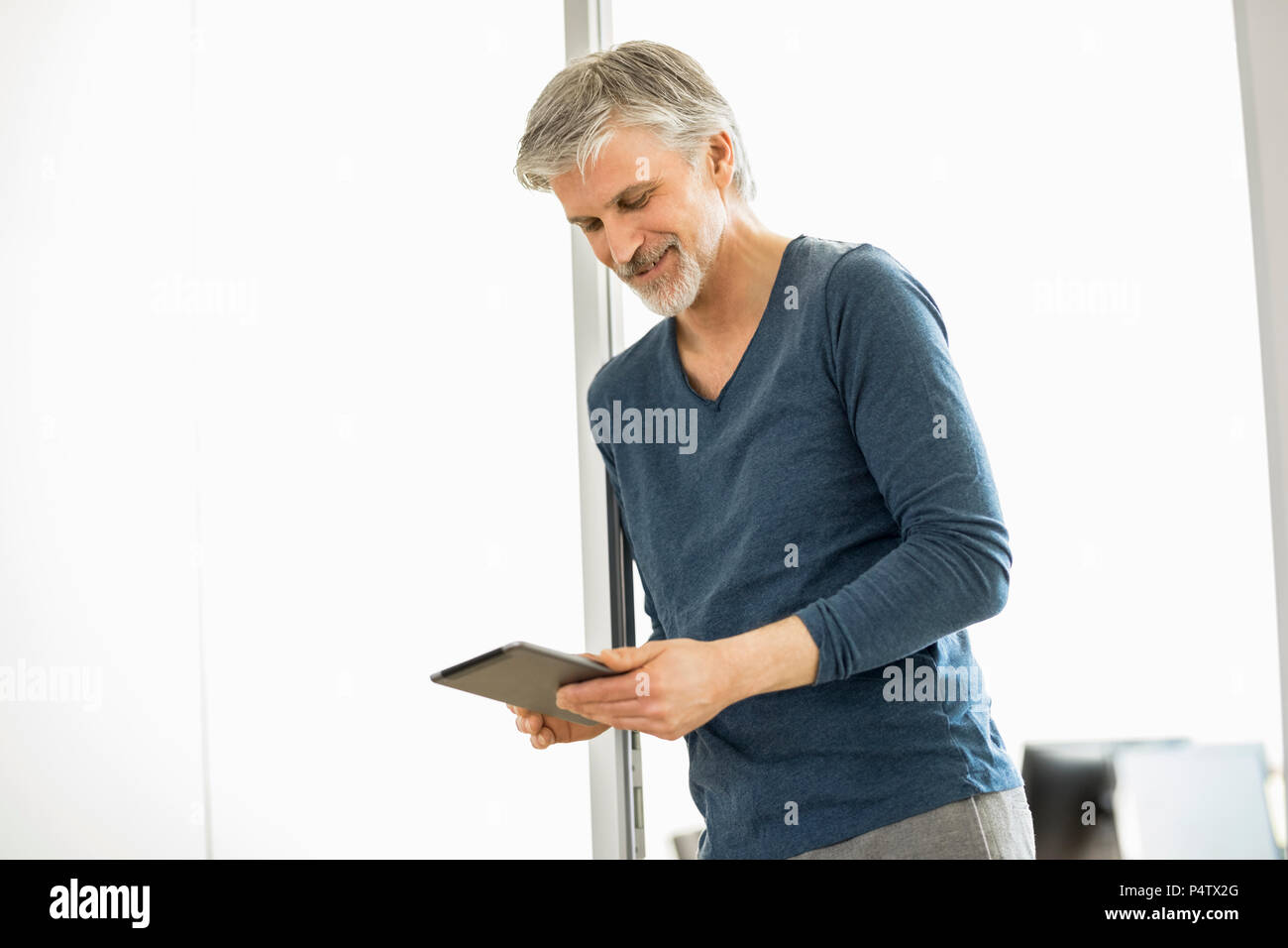 Uomo maturo in piedi nel suo ufficio utilizzando la tavoletta digitale Foto Stock