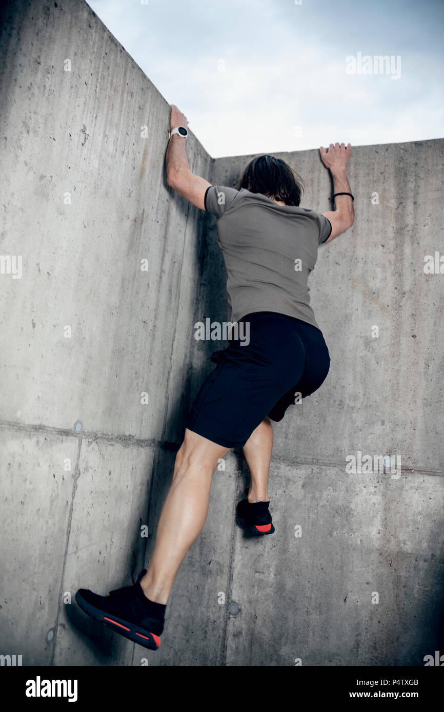 Atleta a salire la parete di calcestruzzo all'aperto Foto Stock