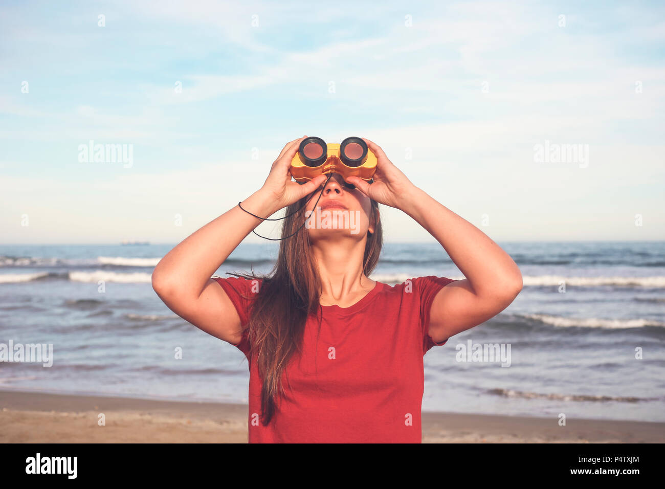 Donna che utilizza un binocolo sulla spiaggia Foto Stock