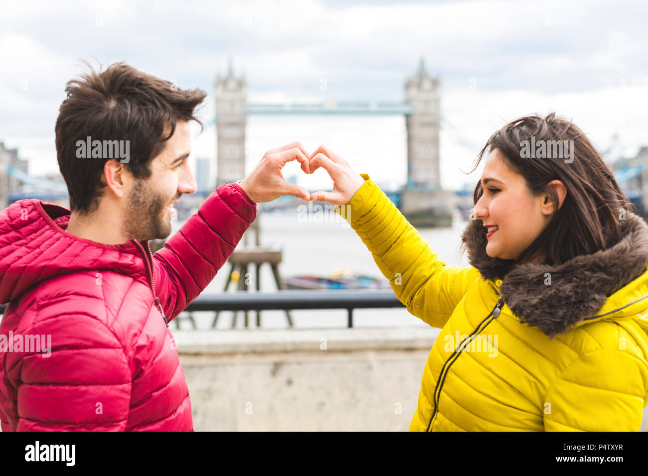 UK, Londra, coppia giovane in piedi sul ponte sul Tamigi la formazione di cuore con le loro mani Foto Stock